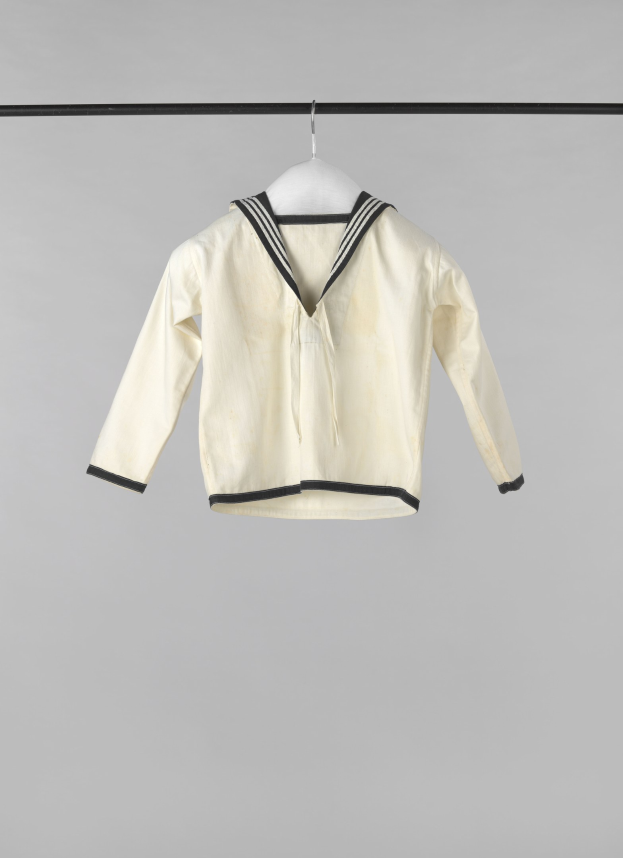 Weißes Seemannsjackett mit Kragen, langen Ärmeln und Knopfleiste, das an einer Wäscheleine gegen einen weißen Hintergrund hängt, aus leichtem Rippenstoff hergestellt.