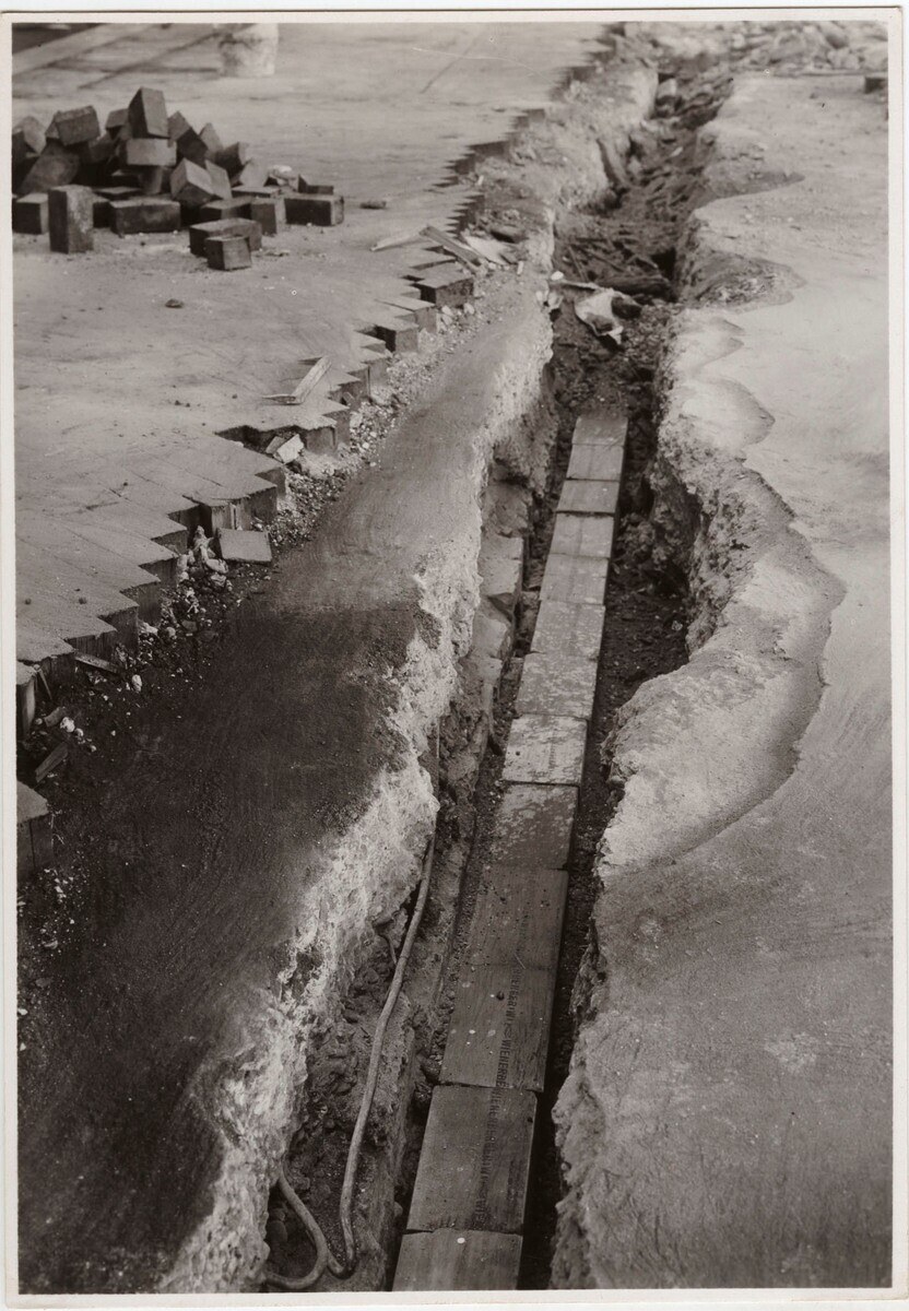 Schwarzes und weißes Foto einer Straße mit einem großen Riss, der hindurchläuft, und verstreuten Ziegelsteinen auf der linken Seite.