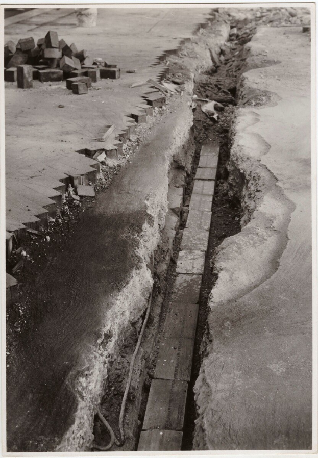 Schwarzes und weißes Foto einer Straße mit einem großen Riss, der hindurchläuft, und verstreuten Ziegelsteinen auf der linken Seite.