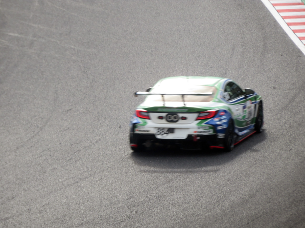 Ein BMW M4 GT3 Rennwagen auf einer Rennstrecke, mit einem Rad im Vordergrund und einer Wand mit Text auf der rechten Seite.