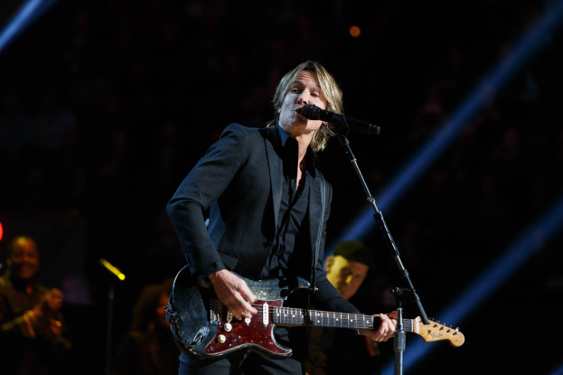 Keith Urban performs on stage at the Joint at Hard Rock Hotel & Casino in Las Vegas, playing guitar with a microphone in front of him and band members in the background under dim lighting.