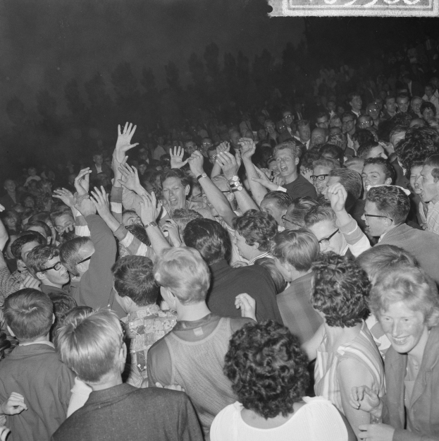 Ein Schwarz-Weiß-Bild einer Konzertmenge mit erhobenen Händen um eine Tafel mit Text.