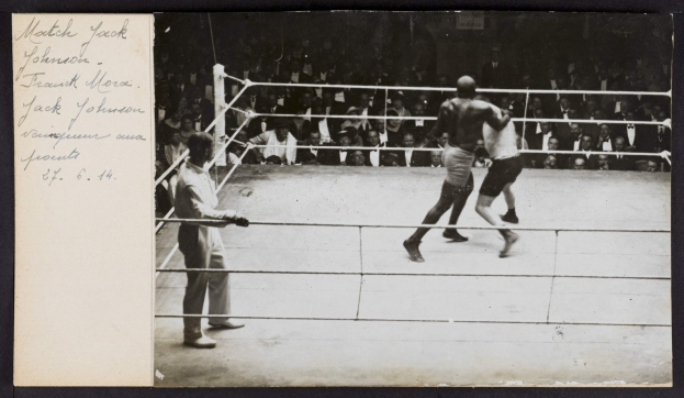 Schwarz-weiß-Foto von zwei Boxern im Ring, ein Referee links daneben und Zuschauer im Hintergrund, mit Text "Jack Johnson vs Frank Morgan" oben links.