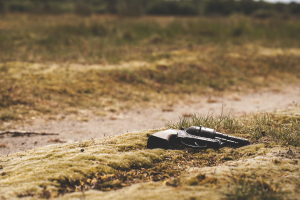 Eine Waffe liegt auf dem Boden in einer grasigen Wiese, umgeben von Bäumen mit einem unscharfen Hintergrund.